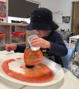 A child with a pumpkin 'pot' adding vinegar